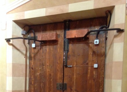 Motorizzazione portone automatico Chiesa con tubazioni a vista e carter di protezione in rame