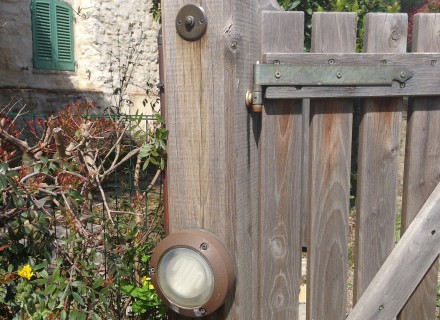 Particolare pulsante campanello in ottone e lampada in Cortem con tubazione in rame su trave cancello in legno